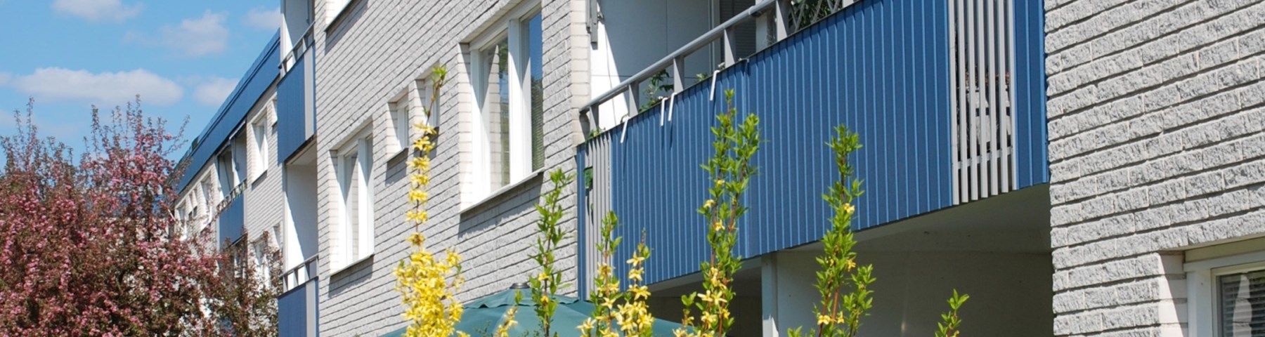 Ekhammars vita bostadshus med blå balkonger och blommande träd